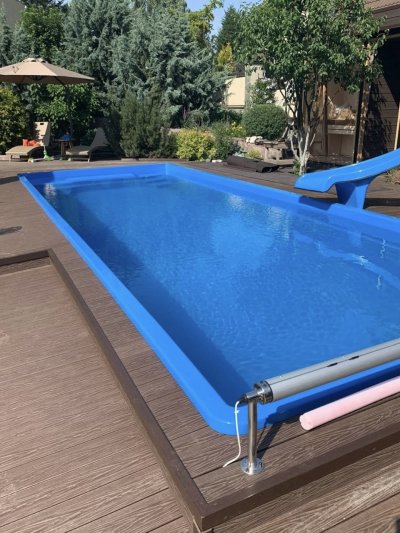 Прямоугольный синий бассейн с террасным настилом, водной горкой и зоной отдыха